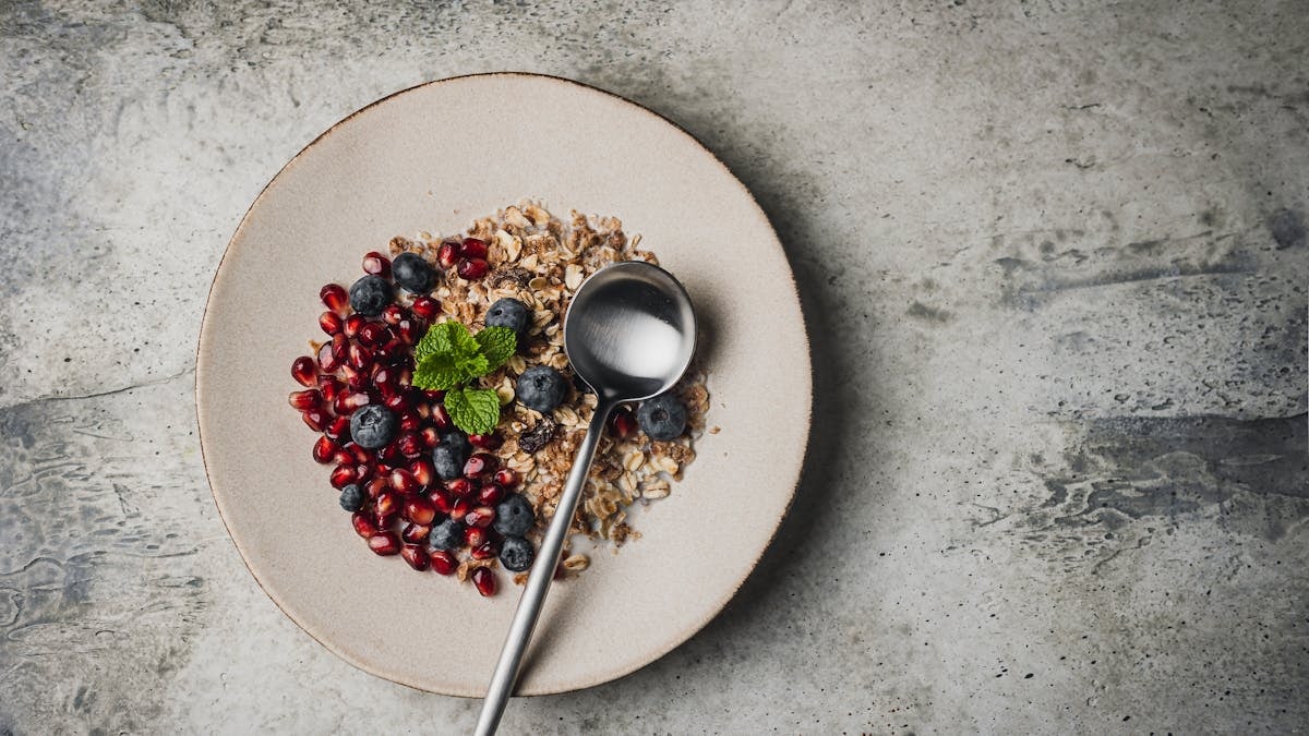 Top view of a healthy breakfast bowl with granola, blueberries, pomegranate seeds, and a spoon on a plate.